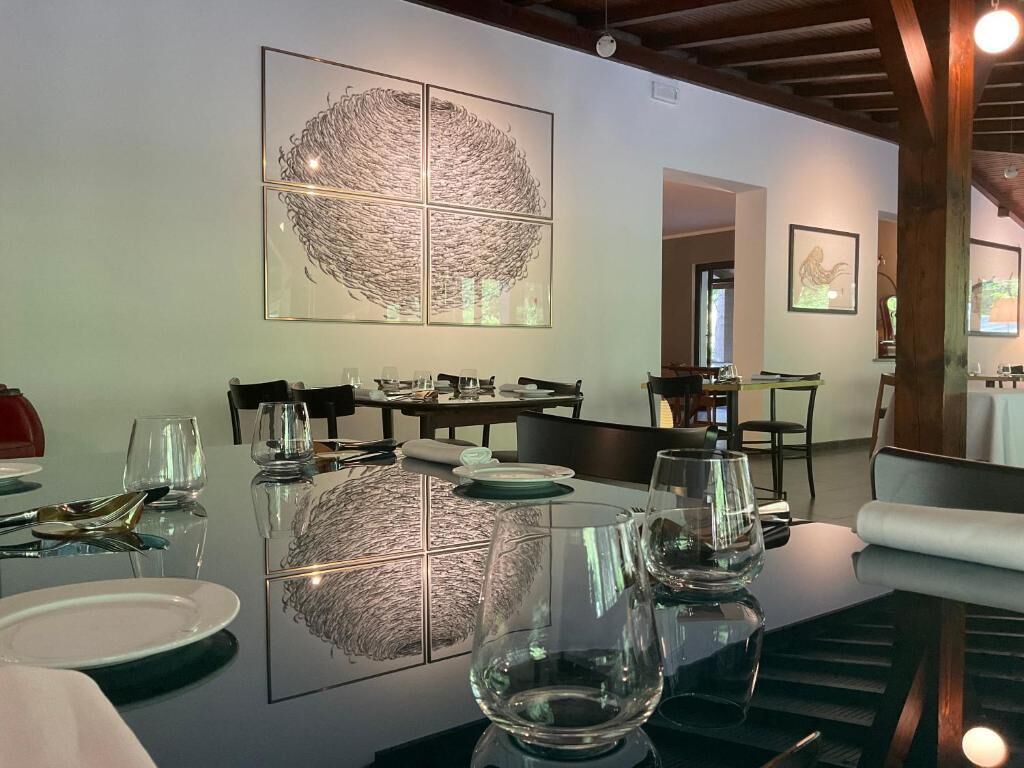 A dining area with a glass table reflecting artwork, chairs, and a wooden ceiling.