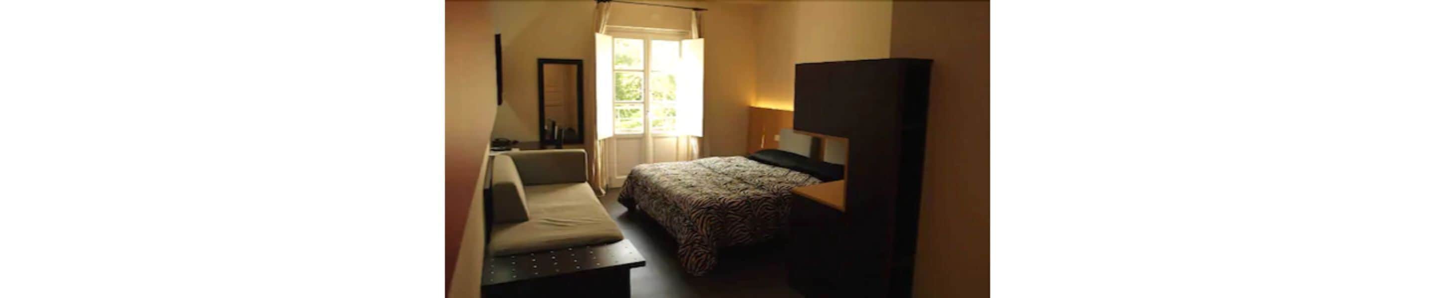 Een kleine, zwak verlichte kamer met een bed, een stoel en een bureau.