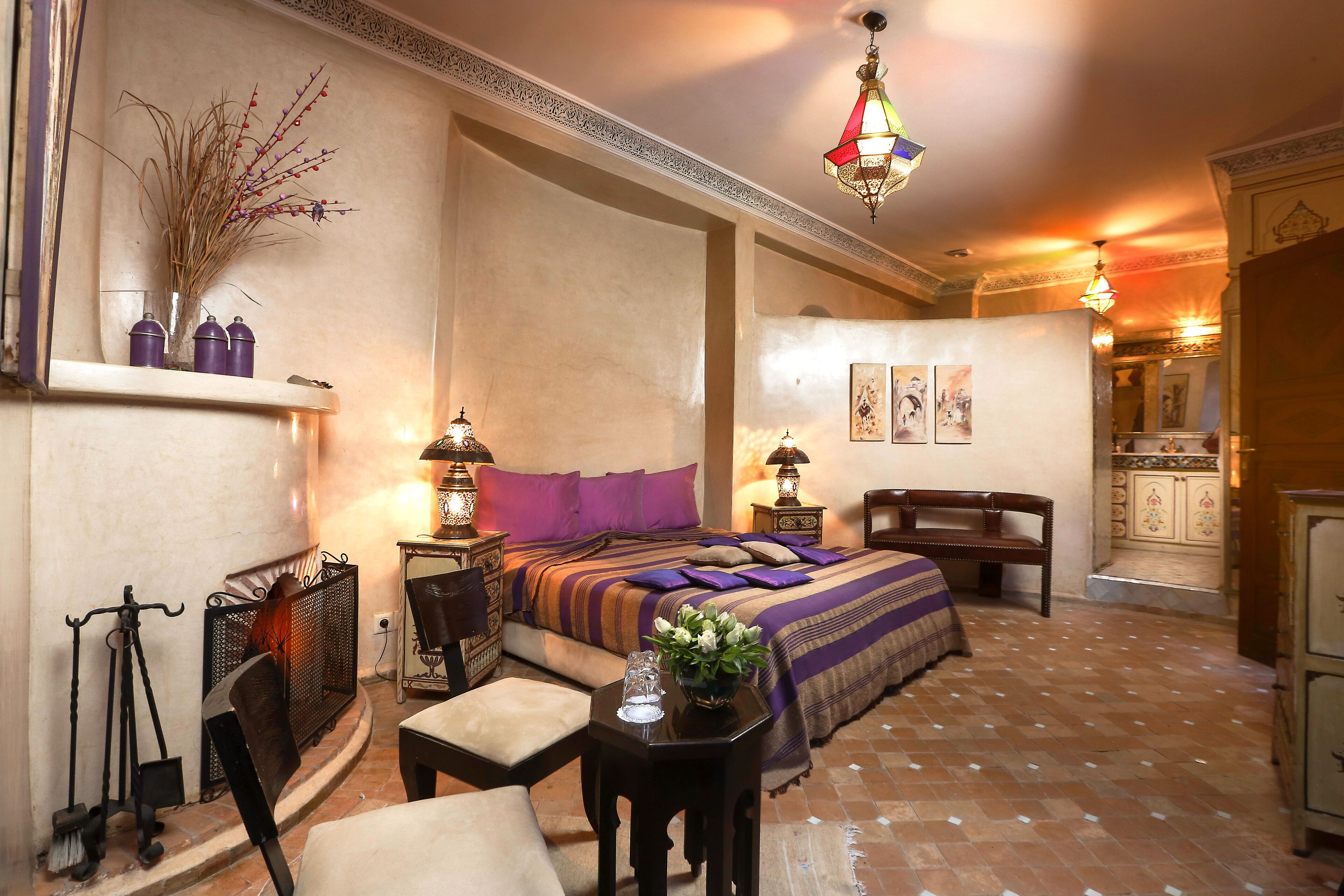 Une chambre élégamment aménagée, dotée d’un grand lit, d’un coin salon avec un fauteuil et une table, ainsi qu’une cheminée.
