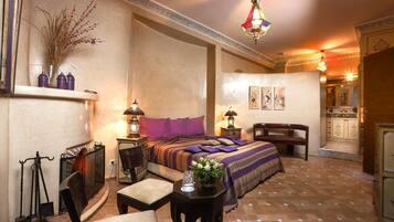 Une chambre élégamment aménagée, dotée d’un grand lit, d’un coin salon avec un fauteuil et une table, ainsi qu’une cheminée.