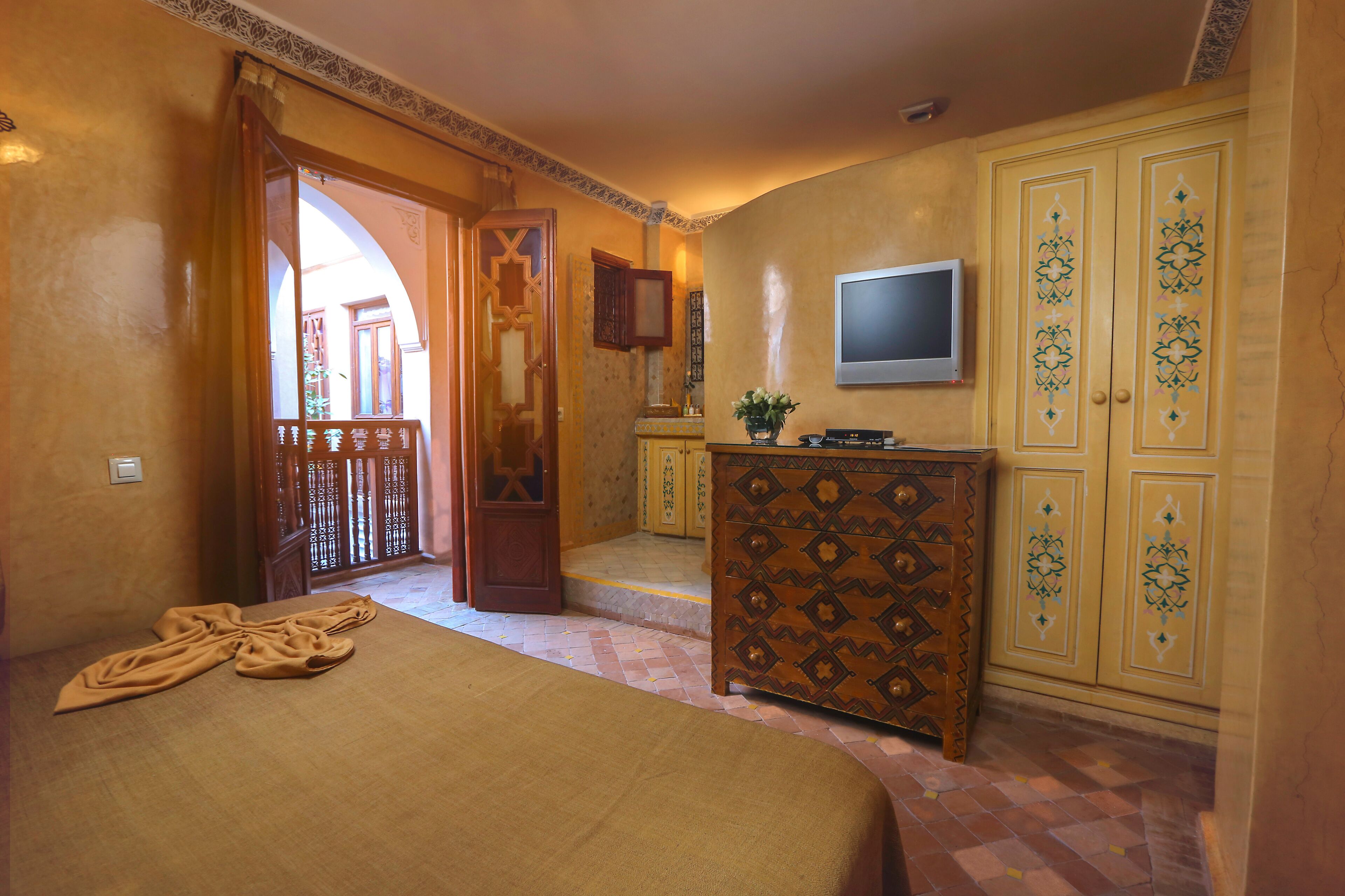 Un dormitorio con cama, cómoda, televisor y puerta que da a un balcón.