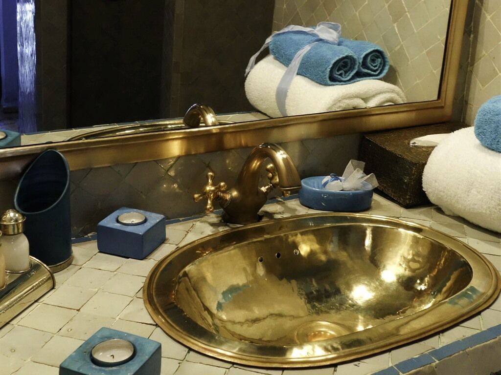 A bathroom with a large gold sink, a mirror, and a towel rack with towels.