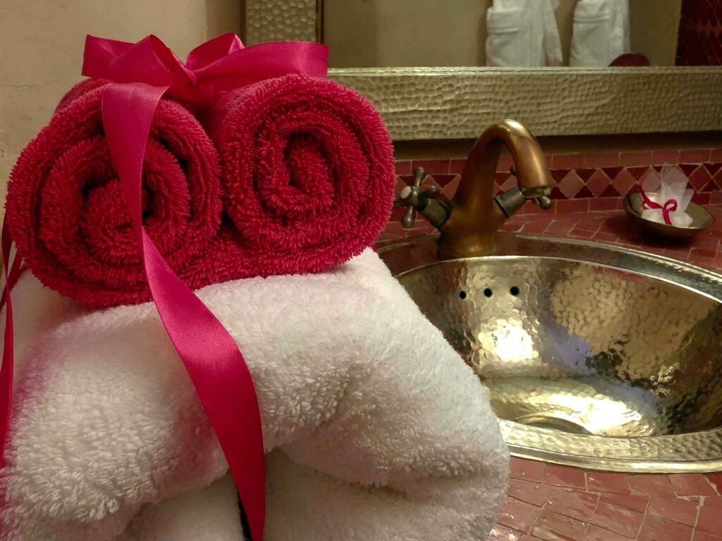 A bathroom with a sink, a mirror, and a towel with a pink ribbon.