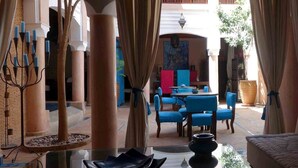 Una hall d'albergo con un'area salotto centrale, una lampada da terra decorativa e vista sul patio esterno.