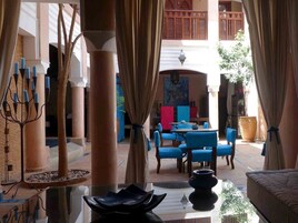 Una hall d'albergo con un'area salotto centrale, una lampada da terra decorativa e vista sul patio esterno.