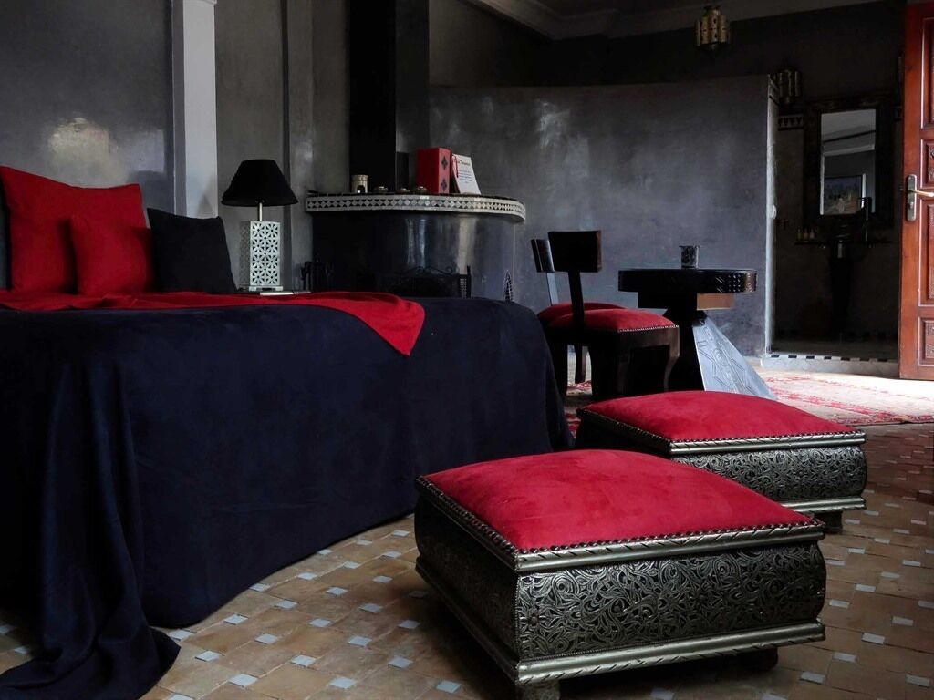 A bedroom with a large bed, red pillows, a side table, and a decorative mirror.