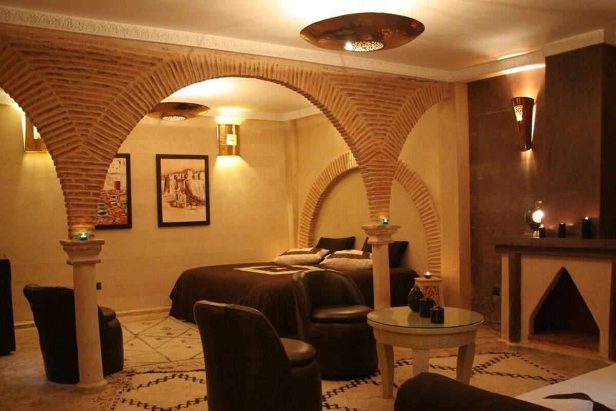 A room with a bed, two chairs, a small table, and a fireplace.