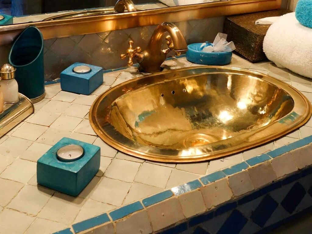 A bathroom with a gold sink, a blue soap dish, and a blue soap dispenser.