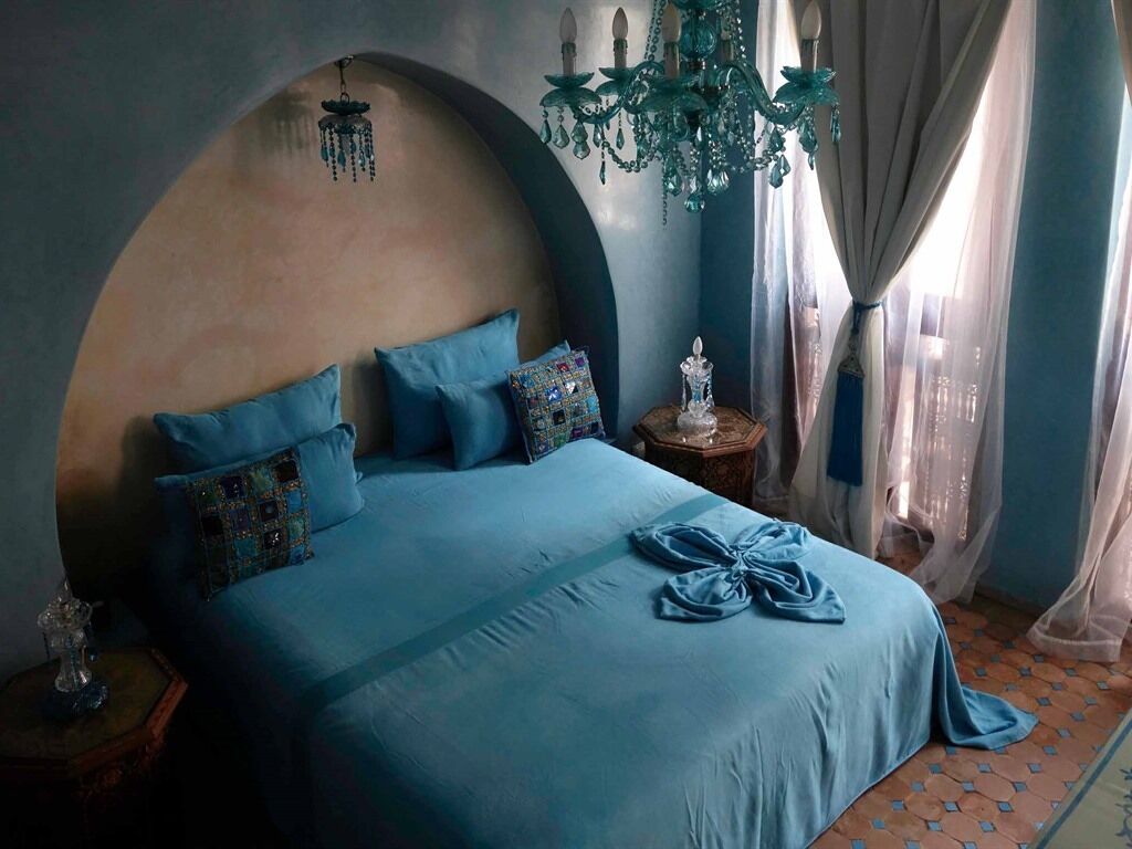 A bedroom with a large bed, a chandelier, and a view of the city through sheer curtains.