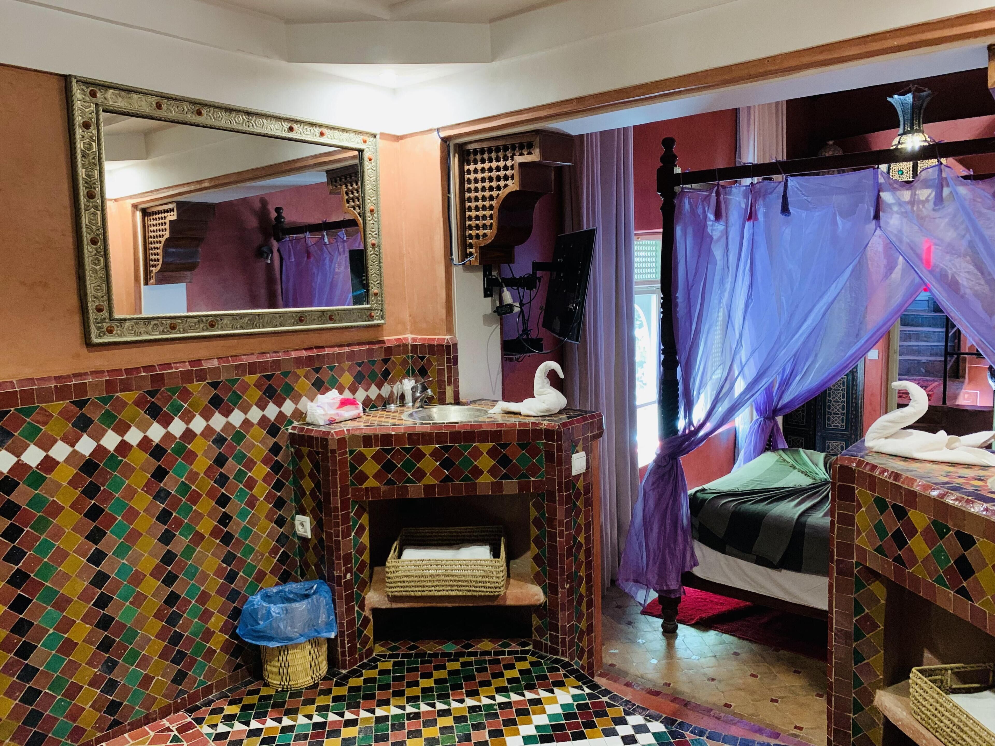 A bathroom with a tiled floor, a sink with a mirror, and a bed with a canopy.