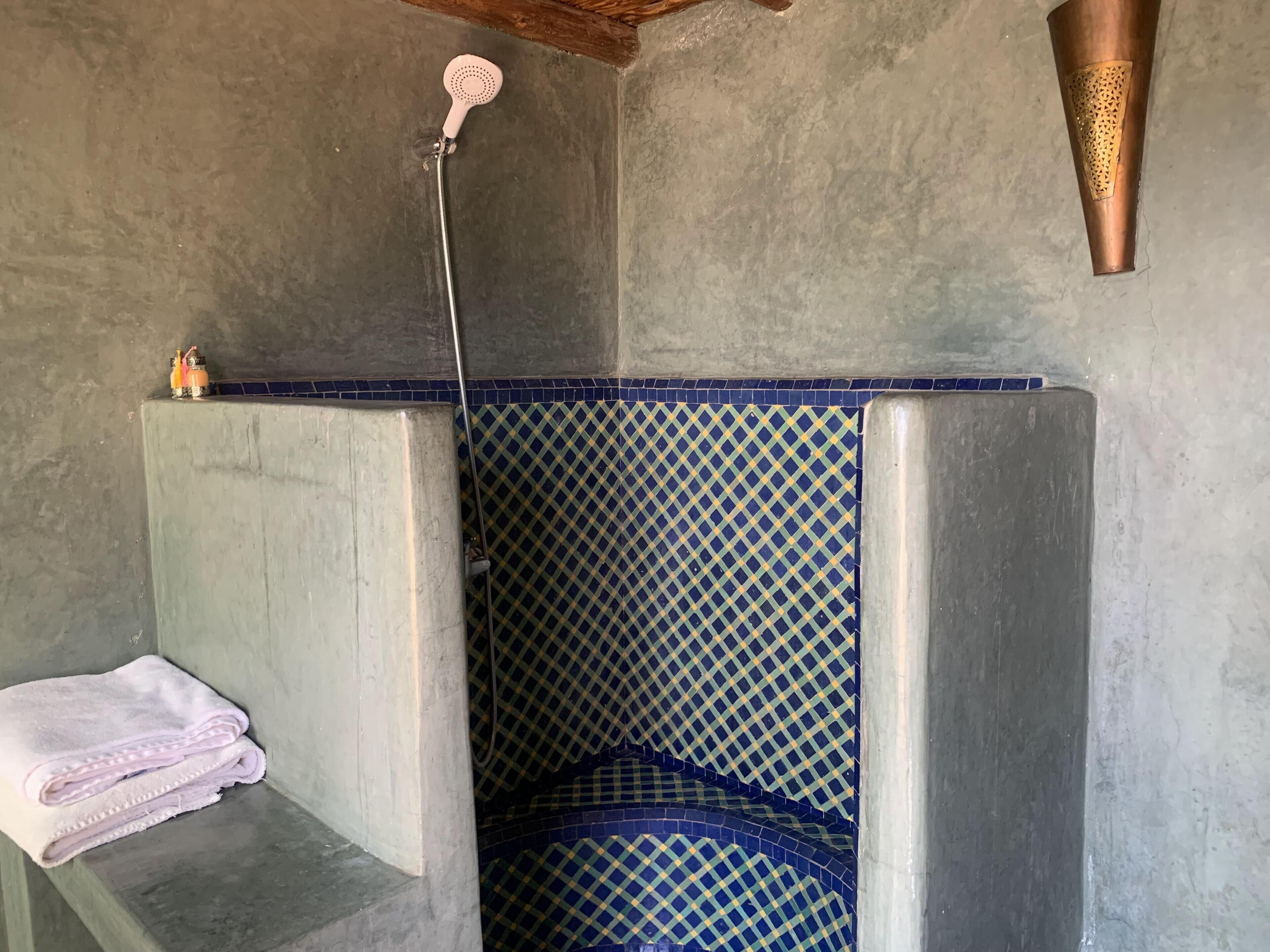 Un baño con ducha, toallero y pared de azulejos estampados.