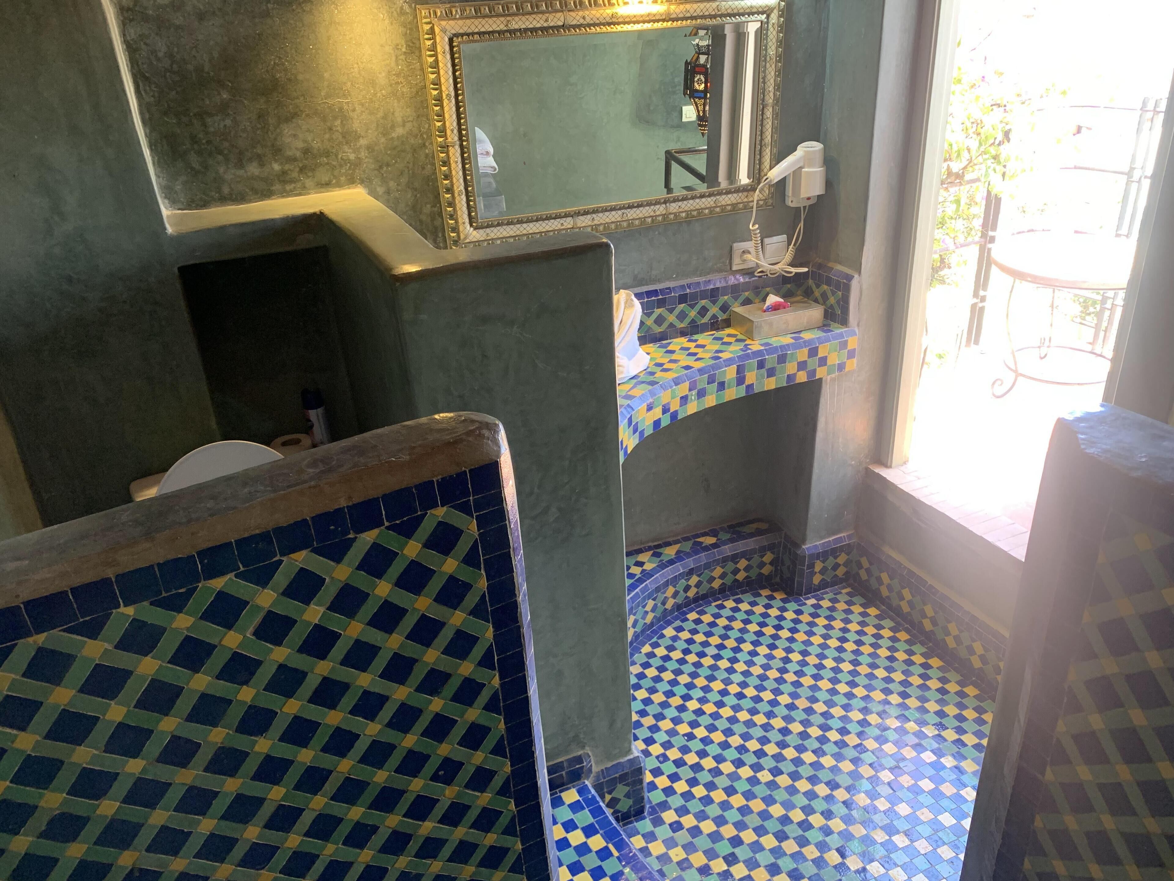Une salle de bain avec des carreaux bleus et verts formant un motif à carreaux, un miroir et un sèche-cheveux fixé au mur.