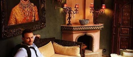 A man sitting on a sofa in a room with a large painting, a fireplace, and a table with a bowl.