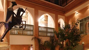 Un área de piscina interior lujosa, con suelo de mármol, un jarrón decorativo y una estatua.