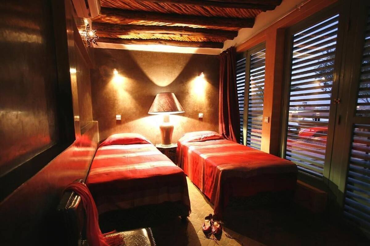 Una habitación con dos camas, una lámpara y una ventana con persianas.