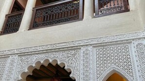 Un edificio de varios niveles con arcos blancos ornamentados y detalles tallados, con balcones de barandilla de hierro forjado e iluminación interior cálida.
