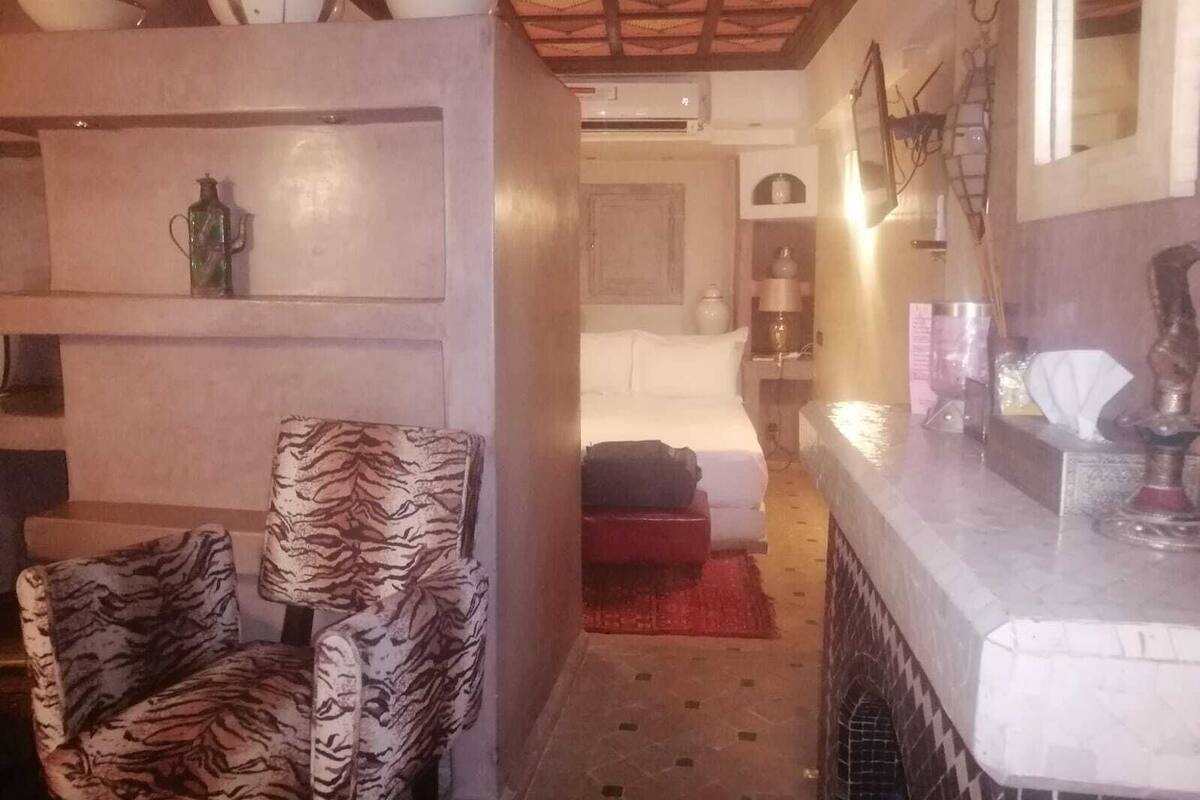 Habitación de hotel con cama, una silla, baño con espejo y una mesita con artículos de tocador.