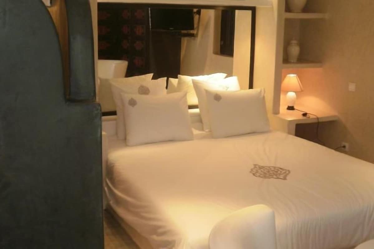 A hotel room with a bed, pillows, a bedside lamp, and a mirror.