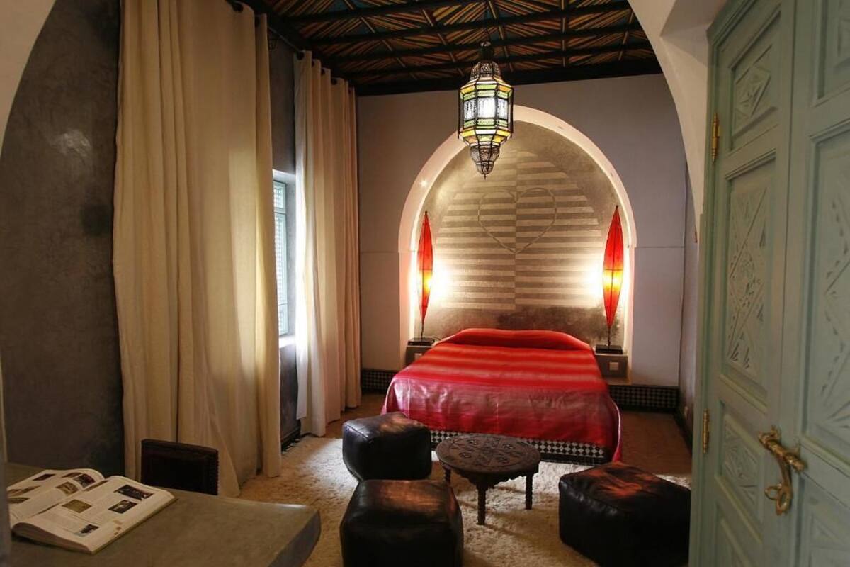 Una habitación con una cama, una mesa con libros, una lámpara y una puerta.