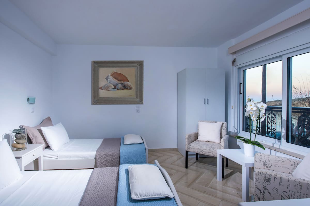 A modern bedroom with two beds, a chair, a table, and a window with a view.