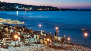 Restaurante à beira-mar com mesas e cadeiras ao ar livre, com vista para um mar tranquilo.