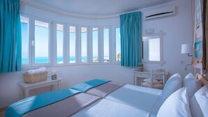 Quarto de hotel com cama, escrivaninha, cadeira e janela com vista para a praia.