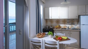 Cozinha com armários brancos, fogão e geladeira. Há uma mesa de jantar com cadeiras e uma janela com cortinas.