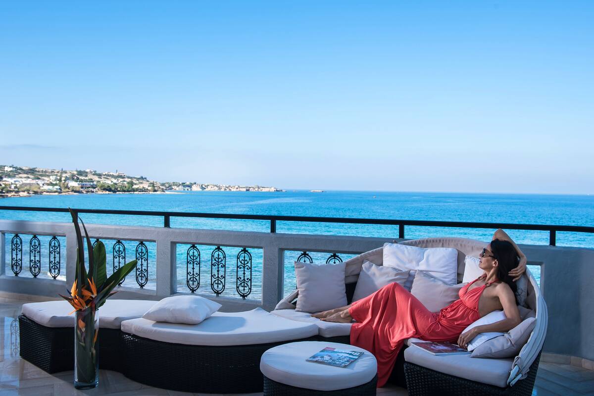 A woman relaxing on a sun lounger with a view of the sea and a distant town.