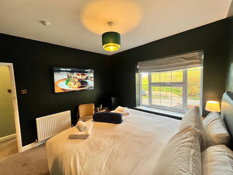 Quarto de hotel com uma cama grande, uma televisão presa à parede, uma janela com vista para o exterior e um radiador no chão.