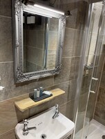 A bathroom with a large ornate mirror, a white sink, and a glass-enclosed shower.