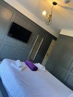 Quarto de hotel com uma cama, televisão de tela plana presa na parede, um espelho e um lustre sobre a cama.