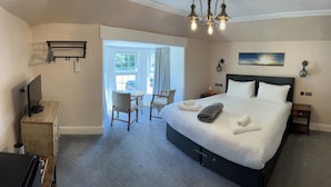 Une chambre d’hôtel avec un grand lit, un bureau avec un ordinateur, une chaise, une petite table et une fenêtre avec des rideaux.