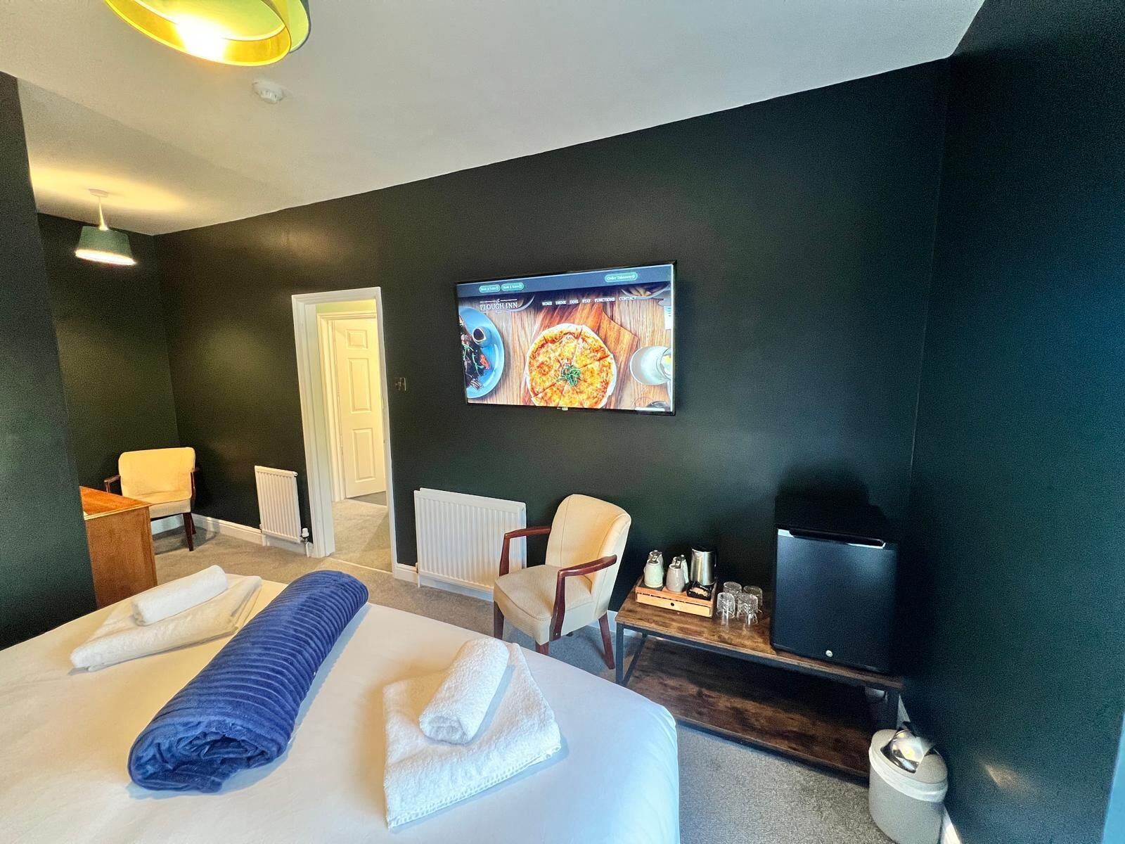 A hotel room with a bed, two chairs, a TV, and a wall-mounted artwork.