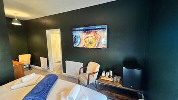 A hotel room with a bed, two chairs, a TV, and a wall-mounted artwork.
