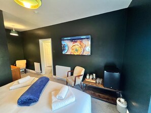 A hotel room with a bed, two chairs, a TV, and a wall-mounted artwork.