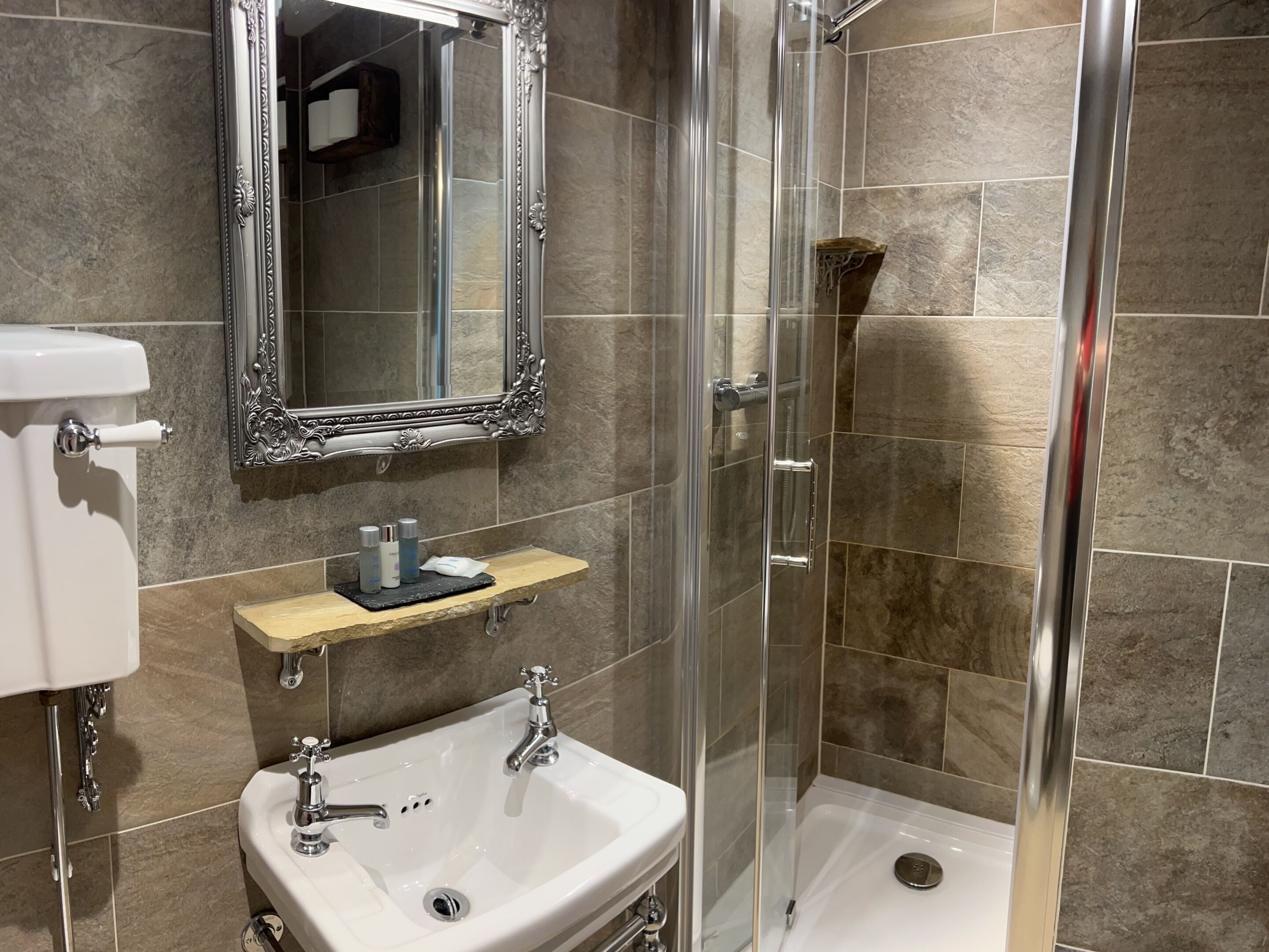 A modern bathroom with a glass-enclosed shower, a white sink with chrome fixtures, and a marble-tiled shower area.