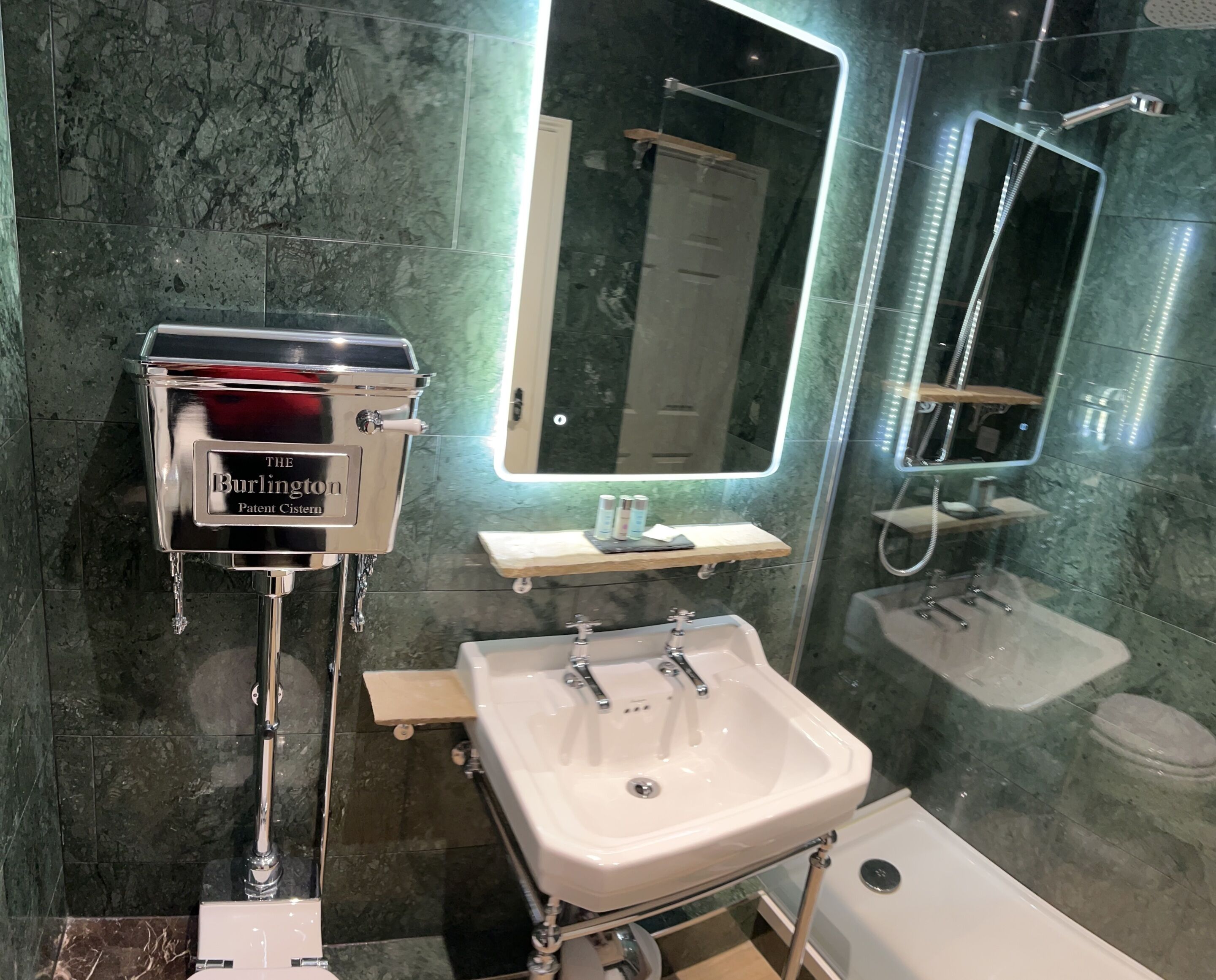 A modern bathroom with a marble backsplash, a white sink, a mirror with LED lights, and a handheld showerhead.