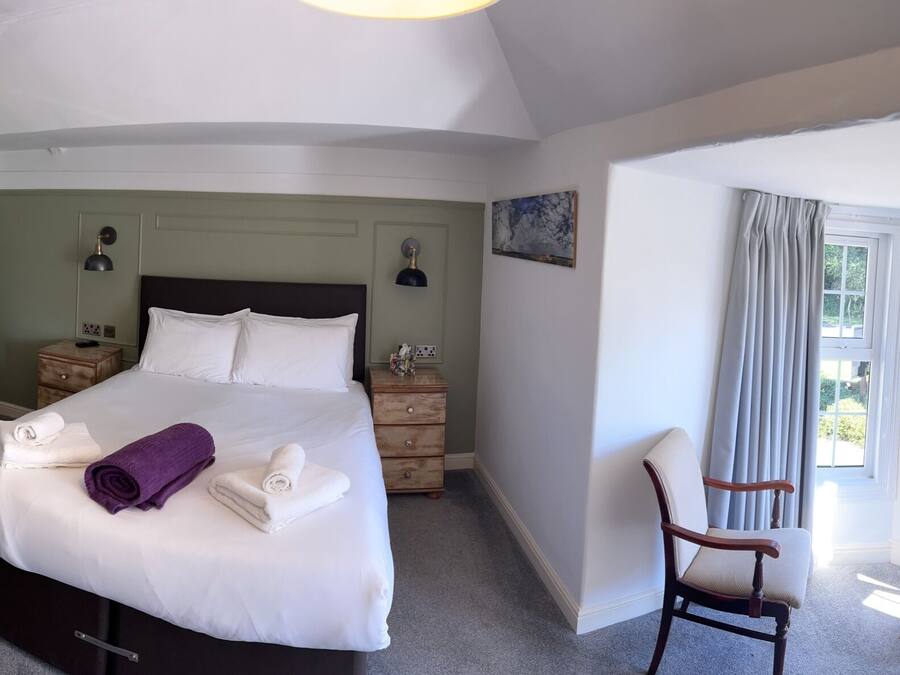 A hotel room with a bed, bedside tables, a chair, a window with curtains, and a radiator.