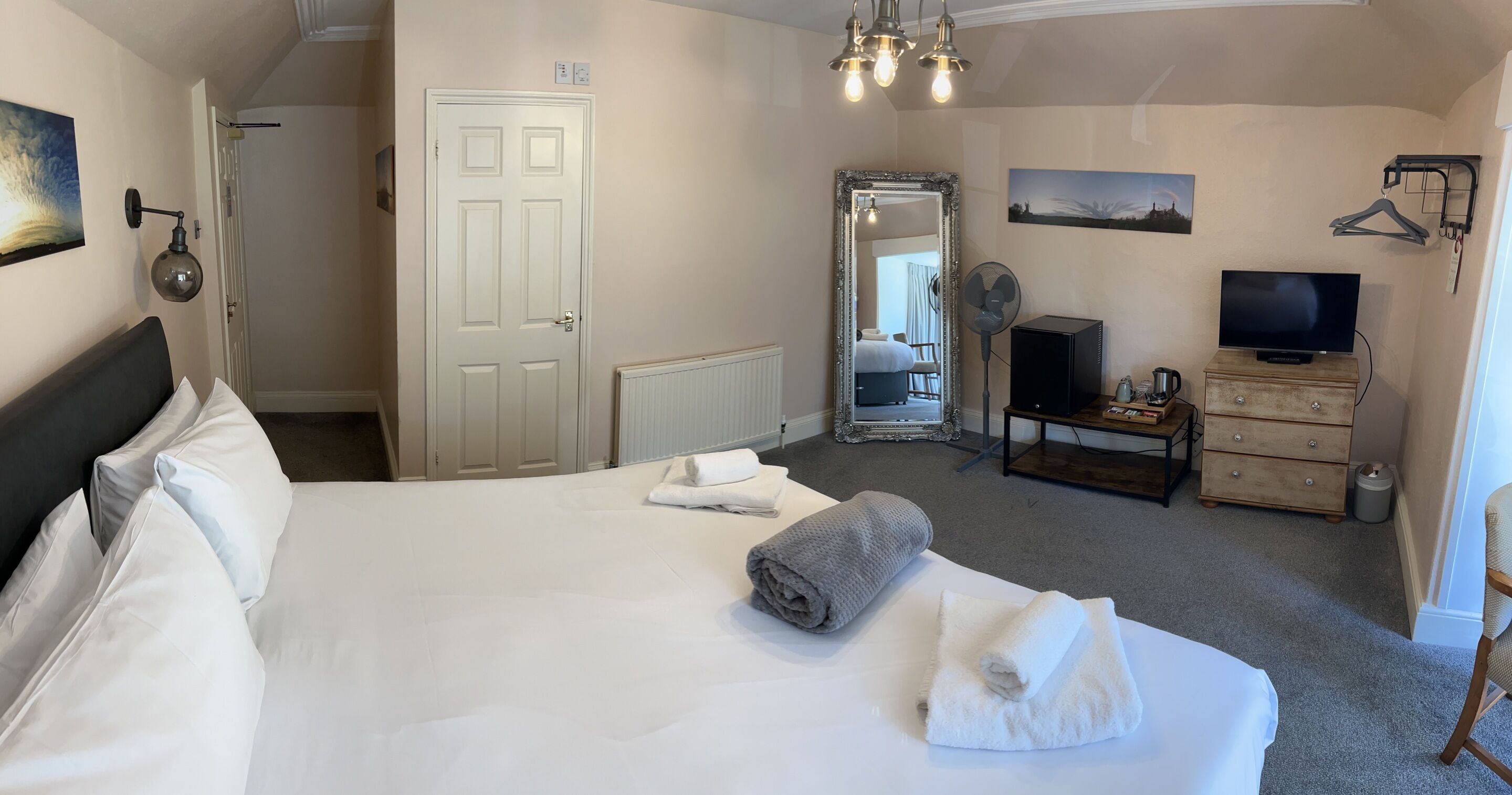 Une chambre d’hôtel avec un grand lit, une commode, une télévision et un miroir.