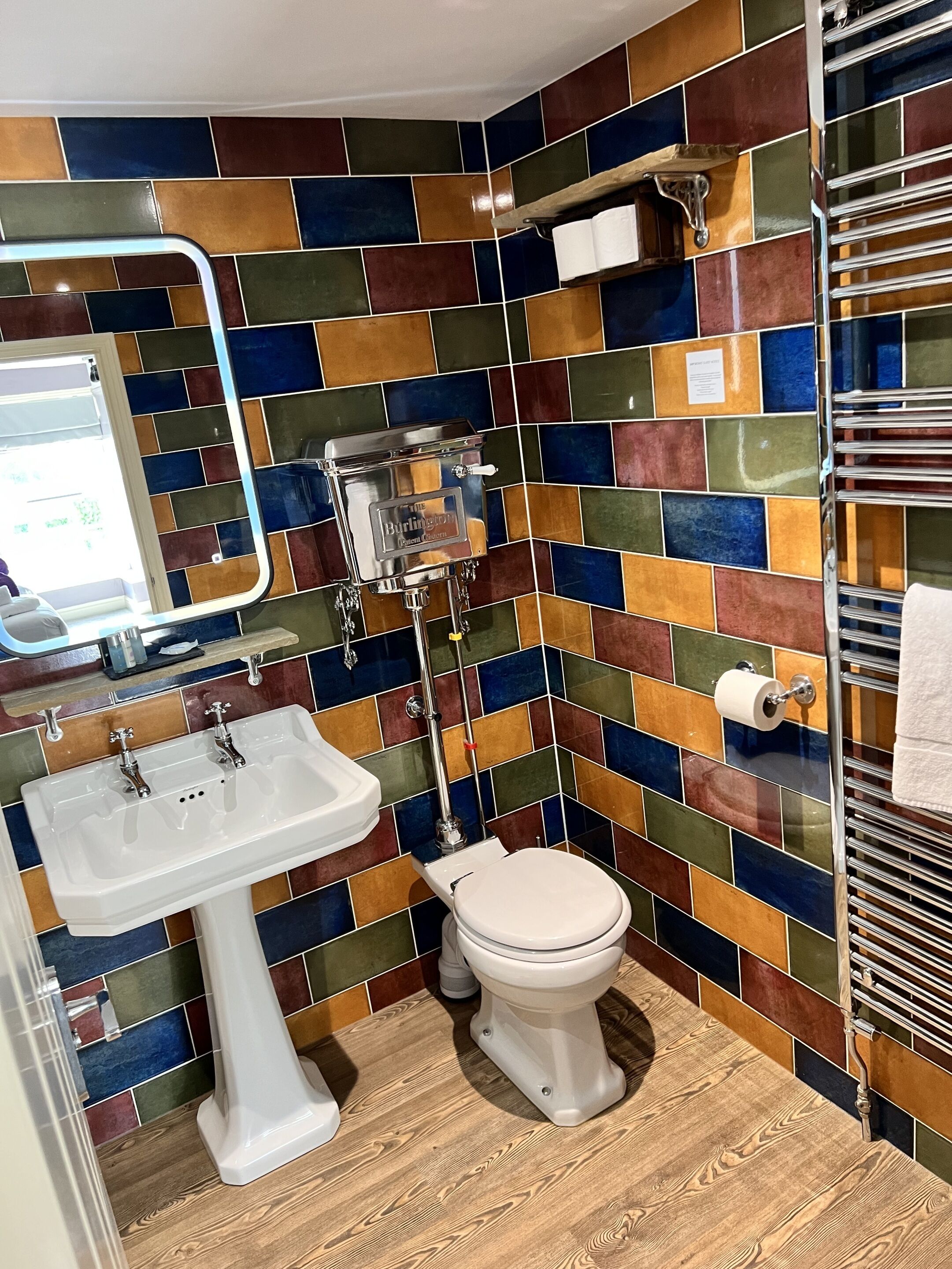 A bathroom with a colorful mosaic tile backsplash, a white sink, a toilet, and a towel rack.