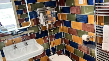 A bathroom with a colorful mosaic tile backsplash, a white sink, a toilet, and a towel rack.