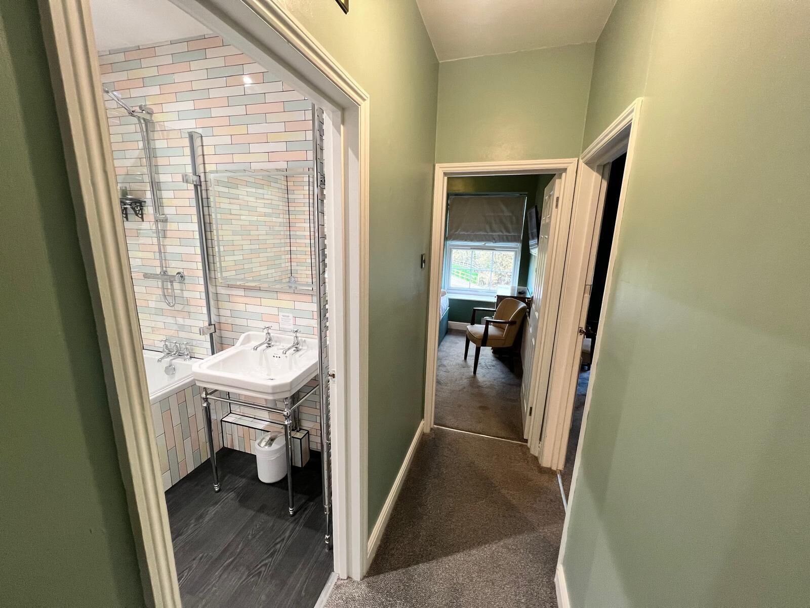 A narrow hallway with a bathroom on the left, featuring a shower, sink, and tiled walls.