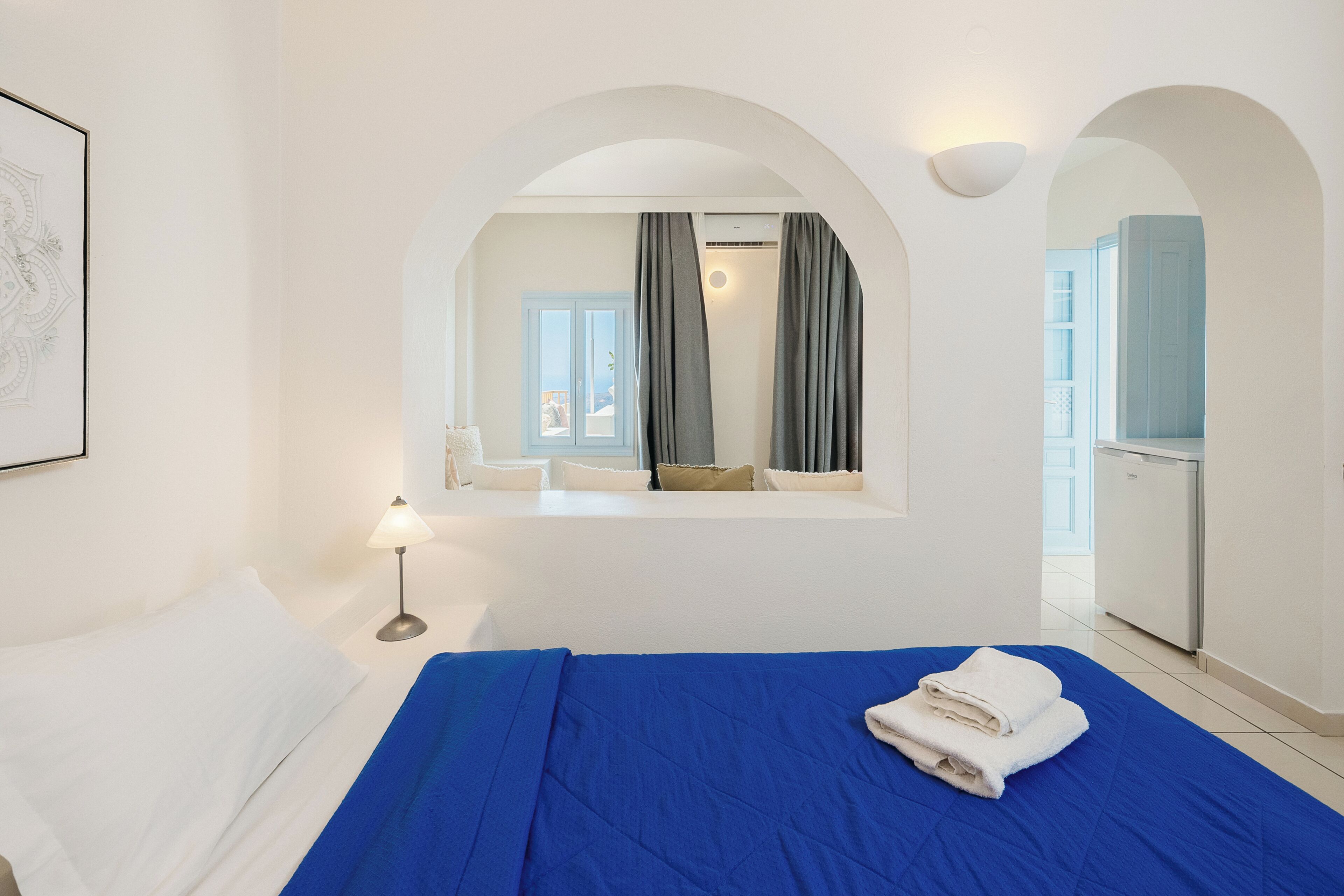 Habitación de hotel con cama, escritorio, lámpara, espejo y vistas al balcón.