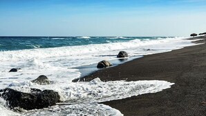 Una platja amb onades que esclaten sobre sorra fosca i roques.