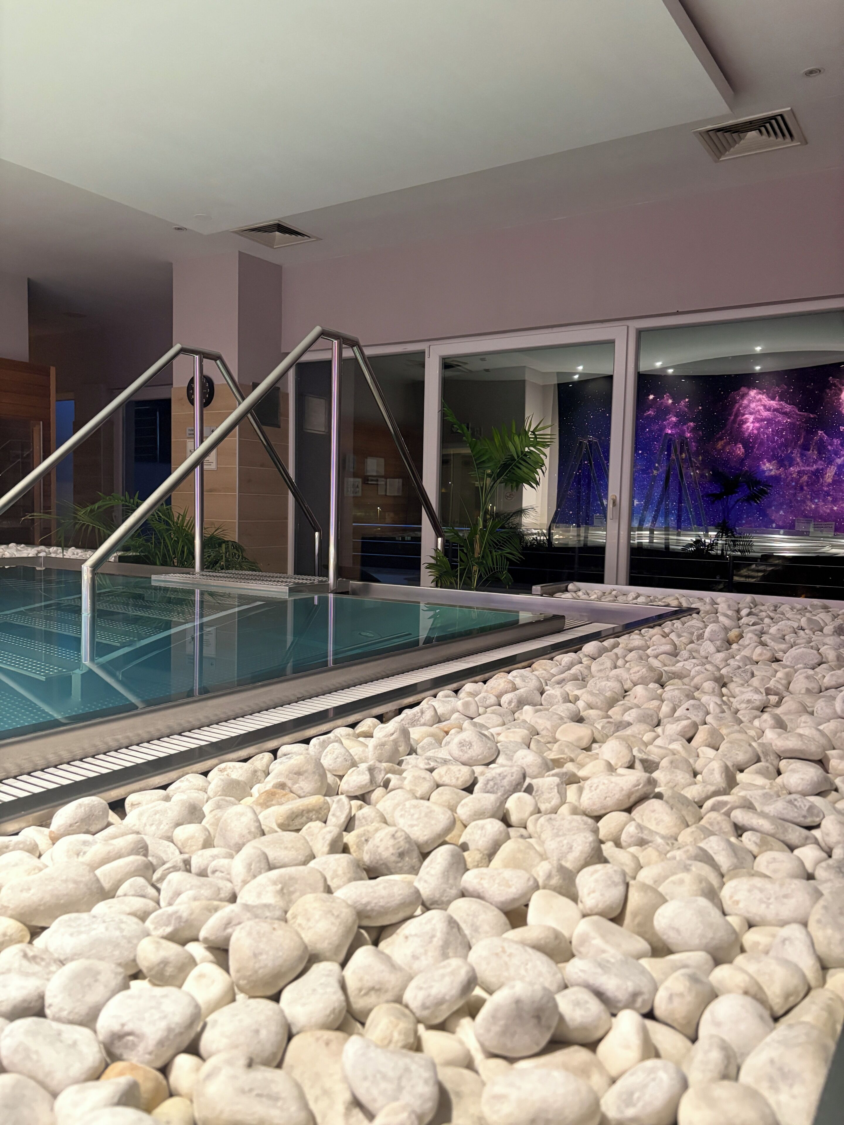 An indoor pool with a pebble floor, a glass barrier, and a wall with a space-themed mural.