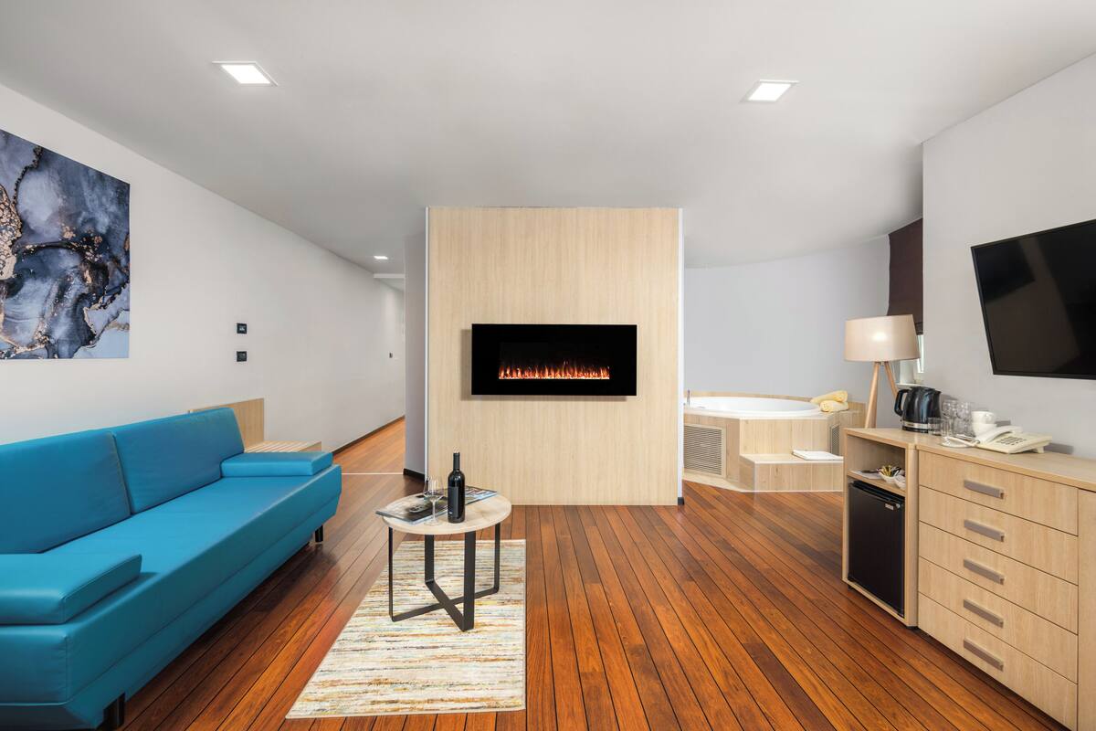 Un salon moderne avec un canapé bleu, un téléviseur à écran plat fixé à un mur en bois, une petite table ronde avec une bouteille et des verres, et un meuble en bois doté de tiroirs.