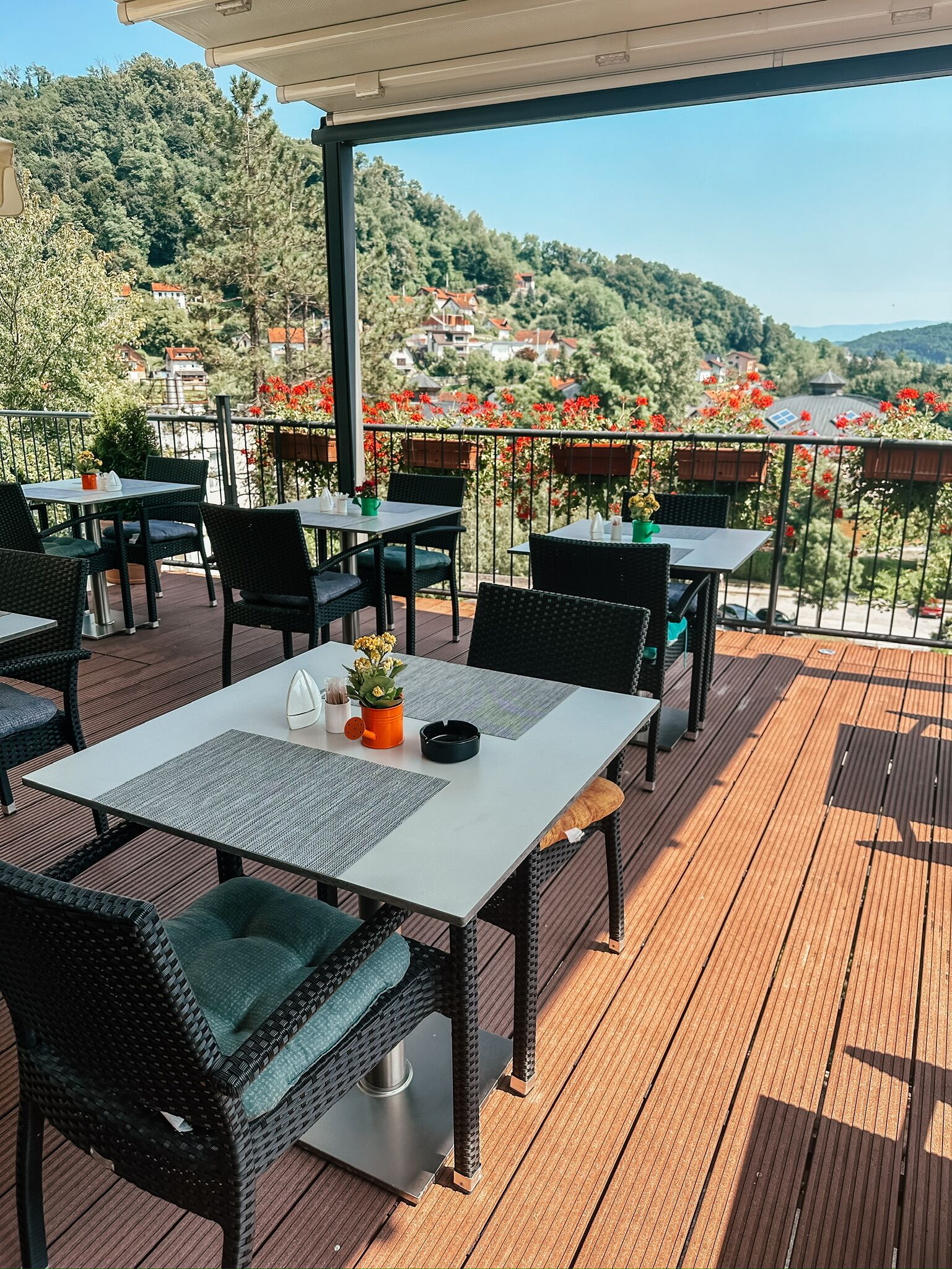 Una terrazza all'aperto con tavoli e sedie, un pergolato e vista su una collina con case.