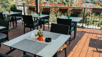 Una terrazza all'aperto con tavoli e sedie, un pergolato e vista su una collina con case.