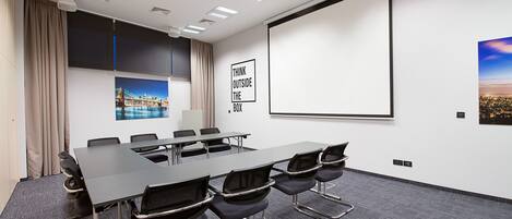 Une salle de conférence équipée d’une grande table, de chaises, d’un écran de projection et d’une affiche motivante.