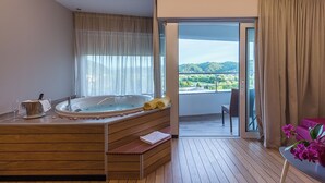 Un baño moderno con una bañera de madera, un banco y un balcón con cerramiento de vidrio que ofrece vistas al verdor.
